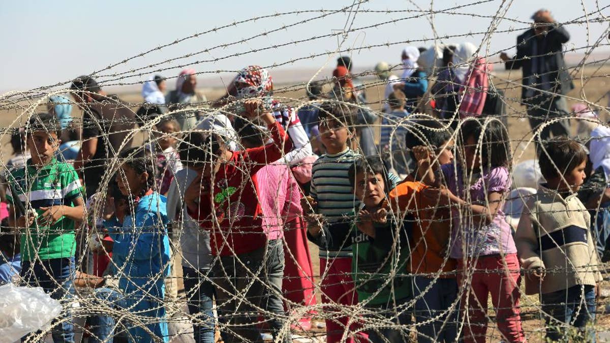 Several hundred Syrian refugees wait to cross into Turkey at the border in Suruc, Turkey, Sunday, Sept. 21, 2014. Turkey opened its border Saturday to allow in up to 60,000 people who massed on the Turkey-Syria border, fleeing the Islamic militants’ advance on Kobani. (AP Photo/Burhan Ozbilici)