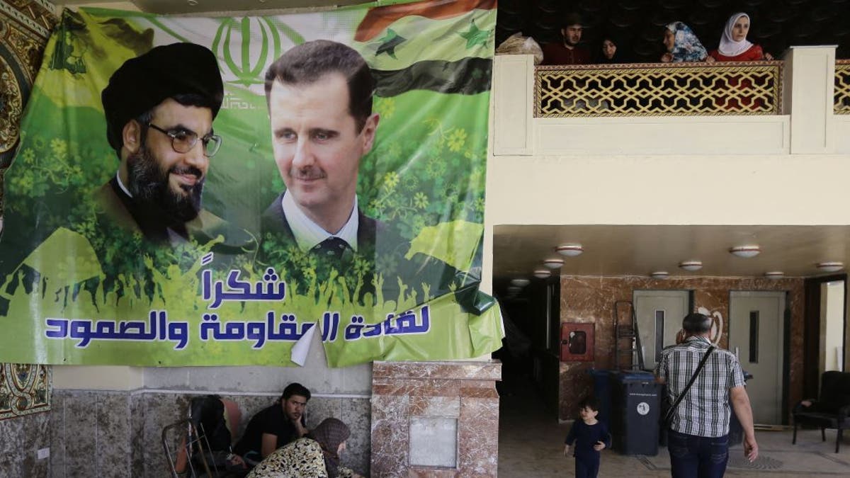 Syrians gather in the lobby of a damaged apartment block, bearing a poster of Syrian President Bashar al-Assad, right, and Hassan Nasrallah, the chief of Lebanon's Shiite movement Hezbollah, following a car bomb near the revered Shiite shrine of Sayyida Zeinab, south of the Syrian capital Damascus on April 25, 2016.