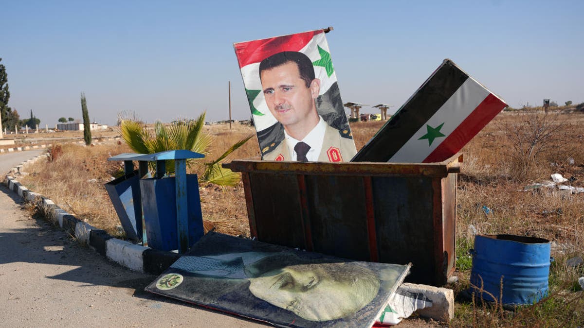 TOPSHOT - A picture taken at the entrance of the Kweyris military airfield in the eastern part of Aleppo province on December 3, 2024 shows a portrait of  Syria's President Bashar al-Assad and a national flag in the garbage dumpster following the take over of the area by rebel groups.