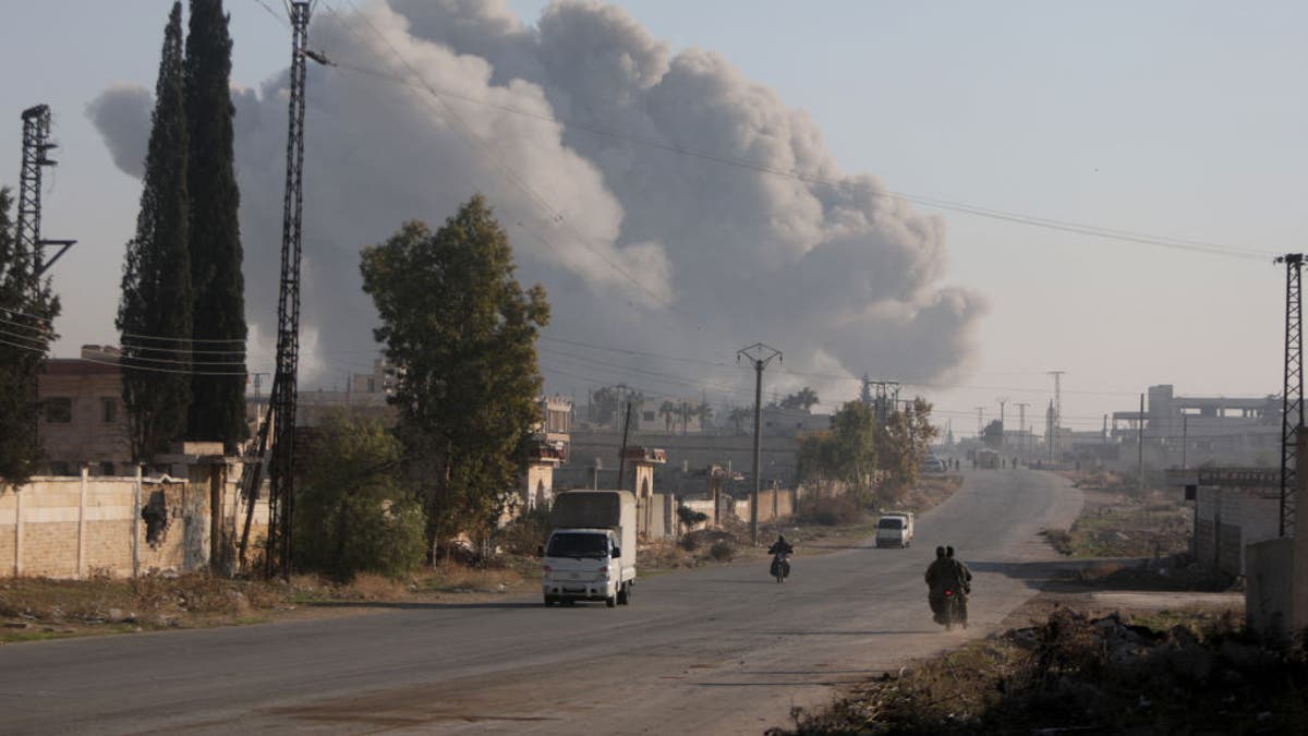 Fighters enter the Rashidin district on the outskirts of Aleppo on their motorbikes with smoke billowing in the background during fighting on Nov. 29, 2024, as Hayat Tahrir al-Sham jihadists and allied factions continue their offensive in the Aleppo province against government forces.