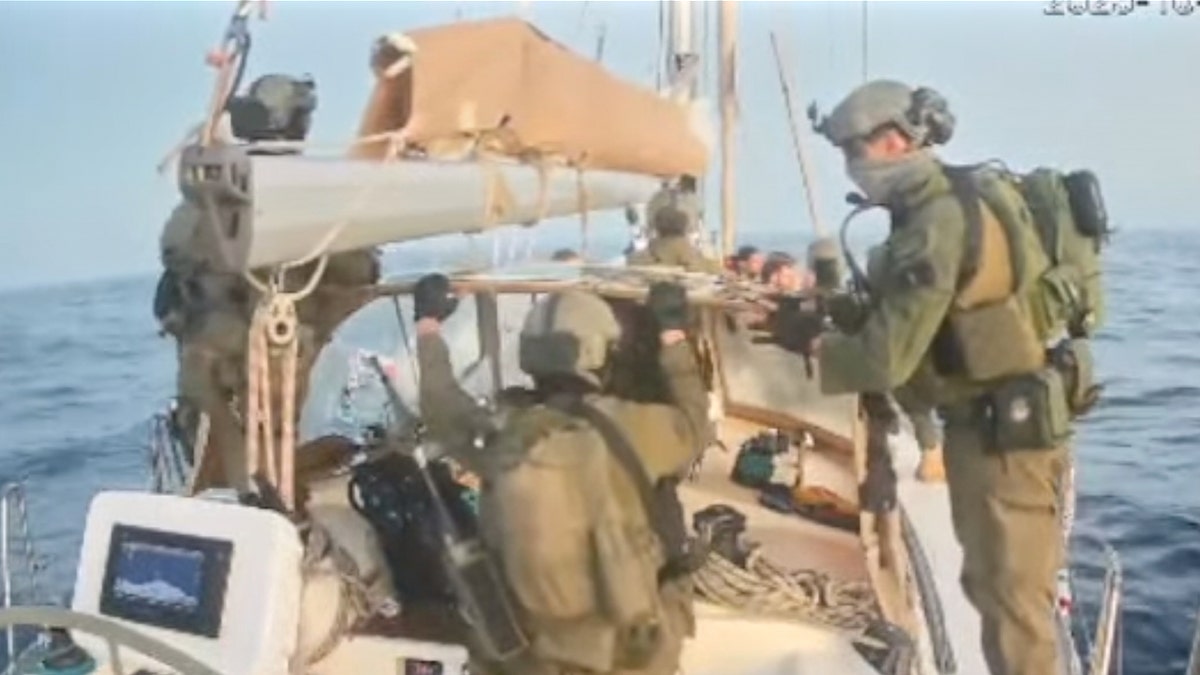 Multiple Israeli soldiers in tactical gear climb onto the deck of a sailboat during an early morning raid.