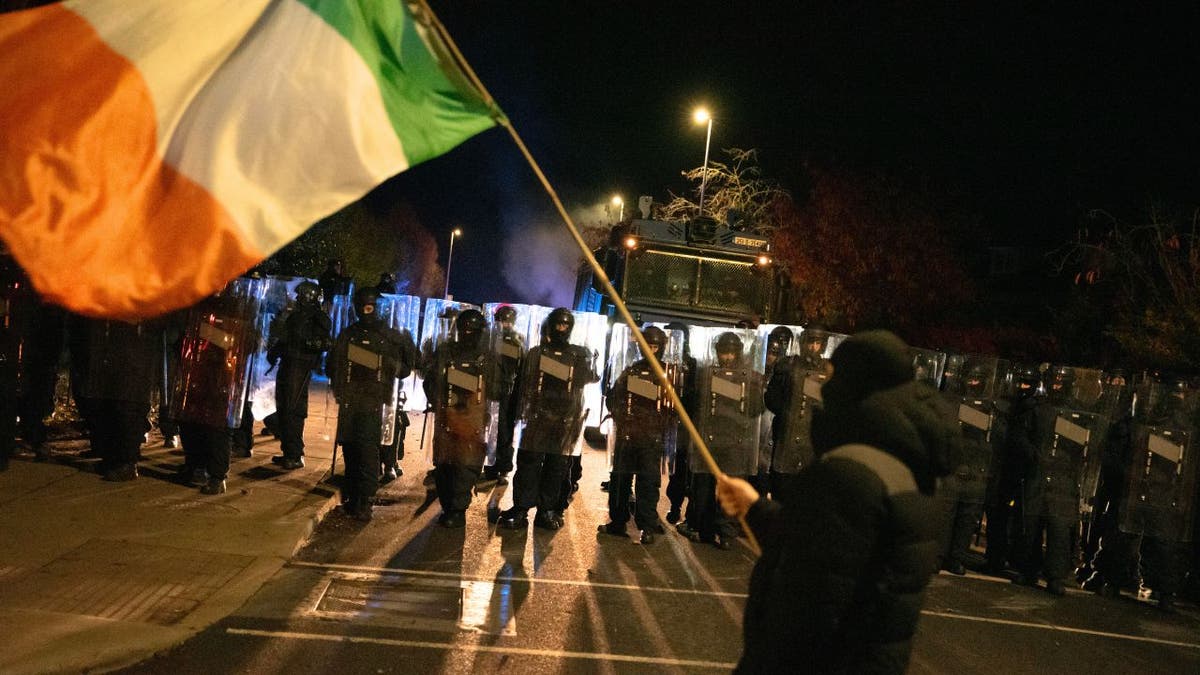 Protester waves Irish flag in front of riot police during Dublin protest.