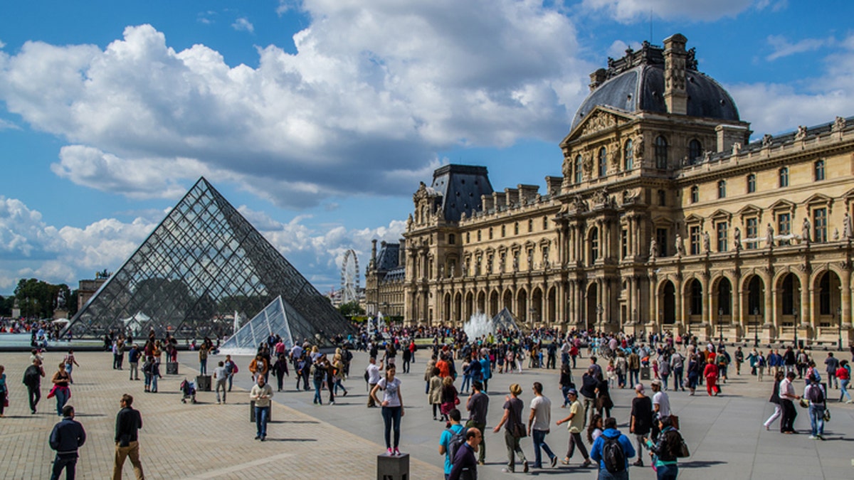 People walking around the outside of the Louvre.