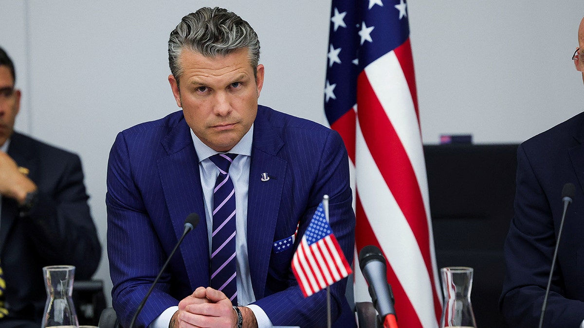 Pete Hegseth sitting and listening with hands folded