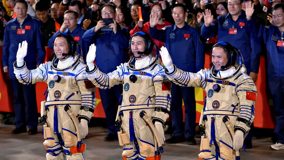 Chinese astronaut for the Shenzhou-21 mission stand and wave in space suits
