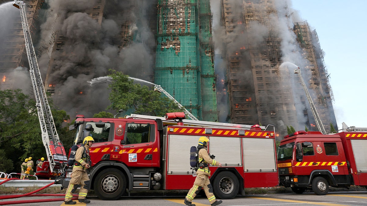 Firefighters work to put out a fire at a burning high-rise apartment complex covered in bamboo scaffolding.