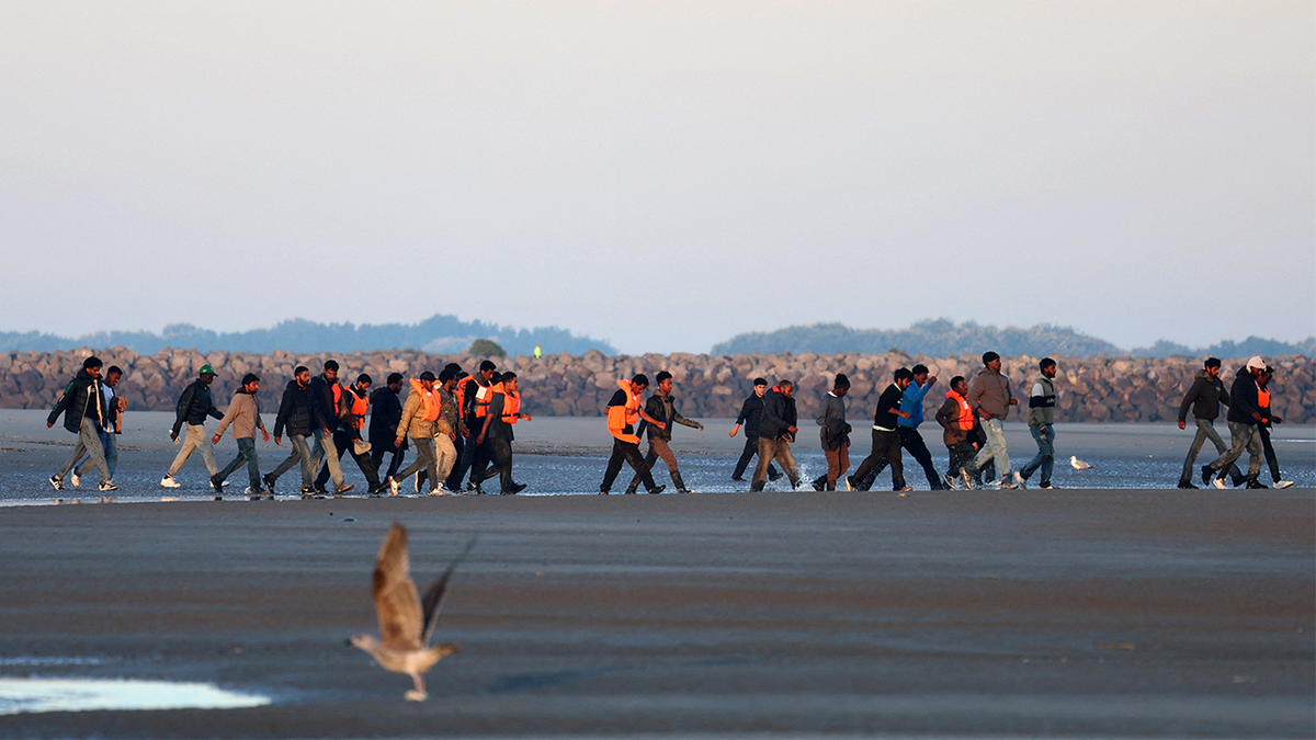 Migrants walk along the beach