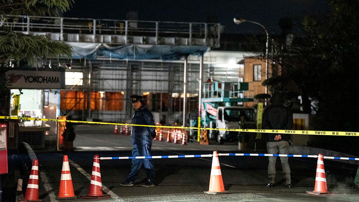 Police officer behind crime scene tape outside factory in Japan