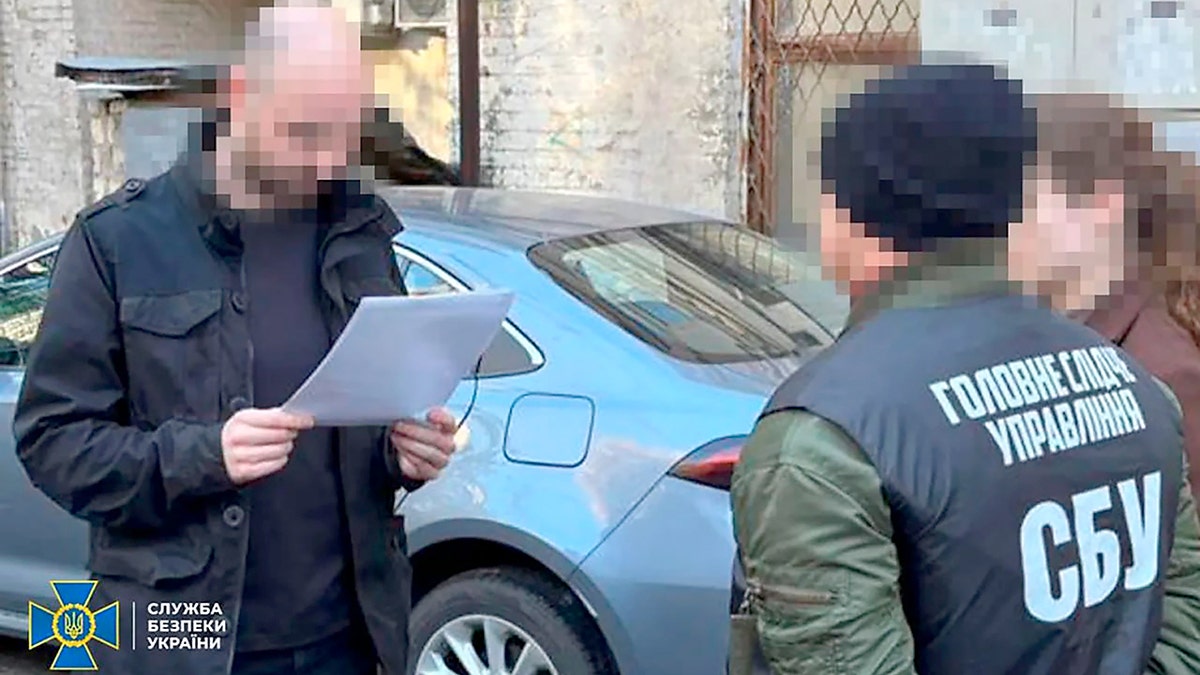 Man holds paper in front of officer. Car is seen in the background.