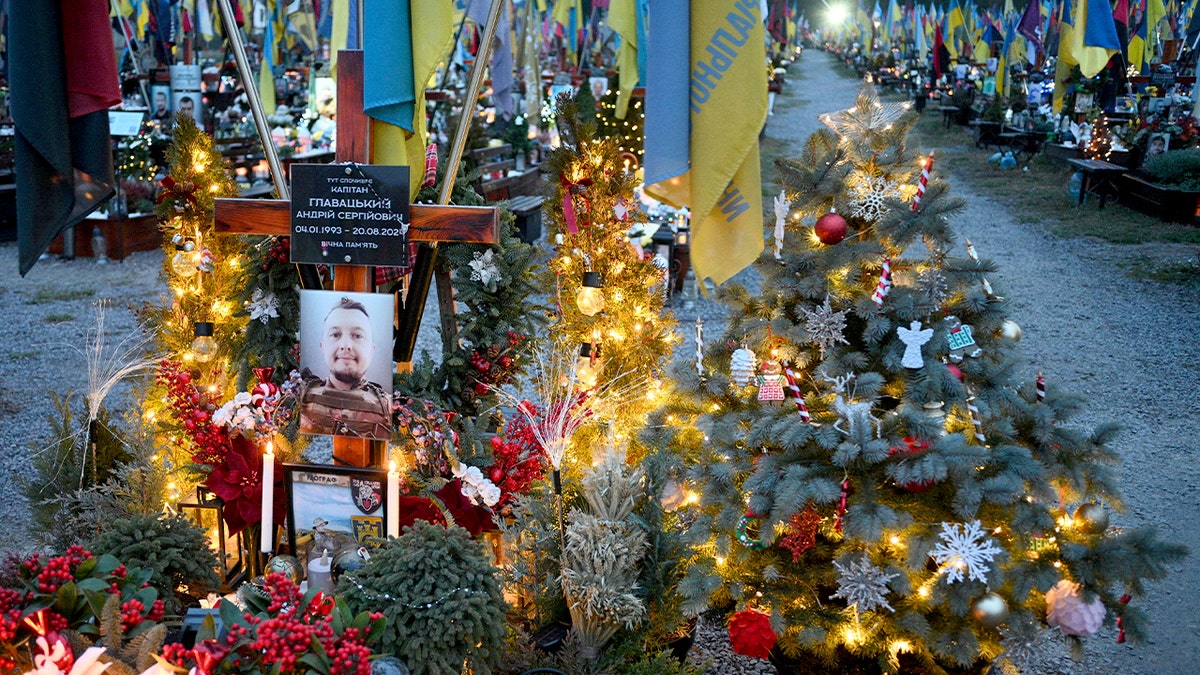 Graves marked with small Christmas trees and holiday decorations line a military cemetery.