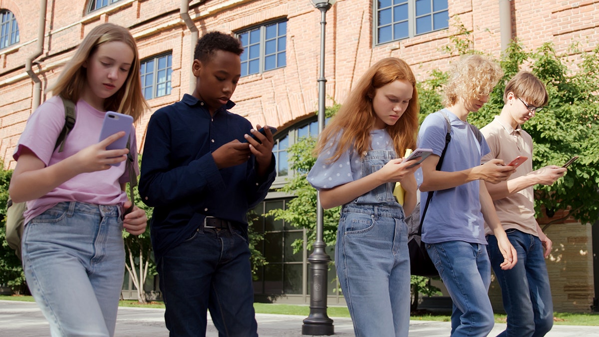 Young students looking at smartphones while walking