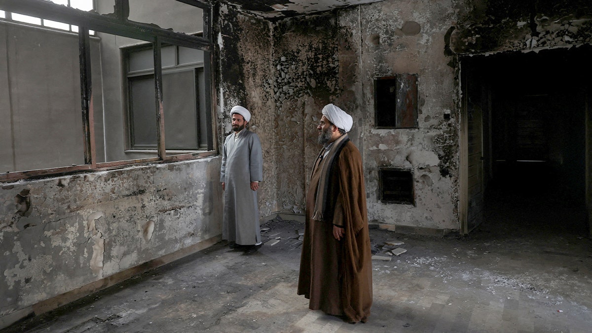 Religious figures stand inside a damaged building with soot-stained walls.