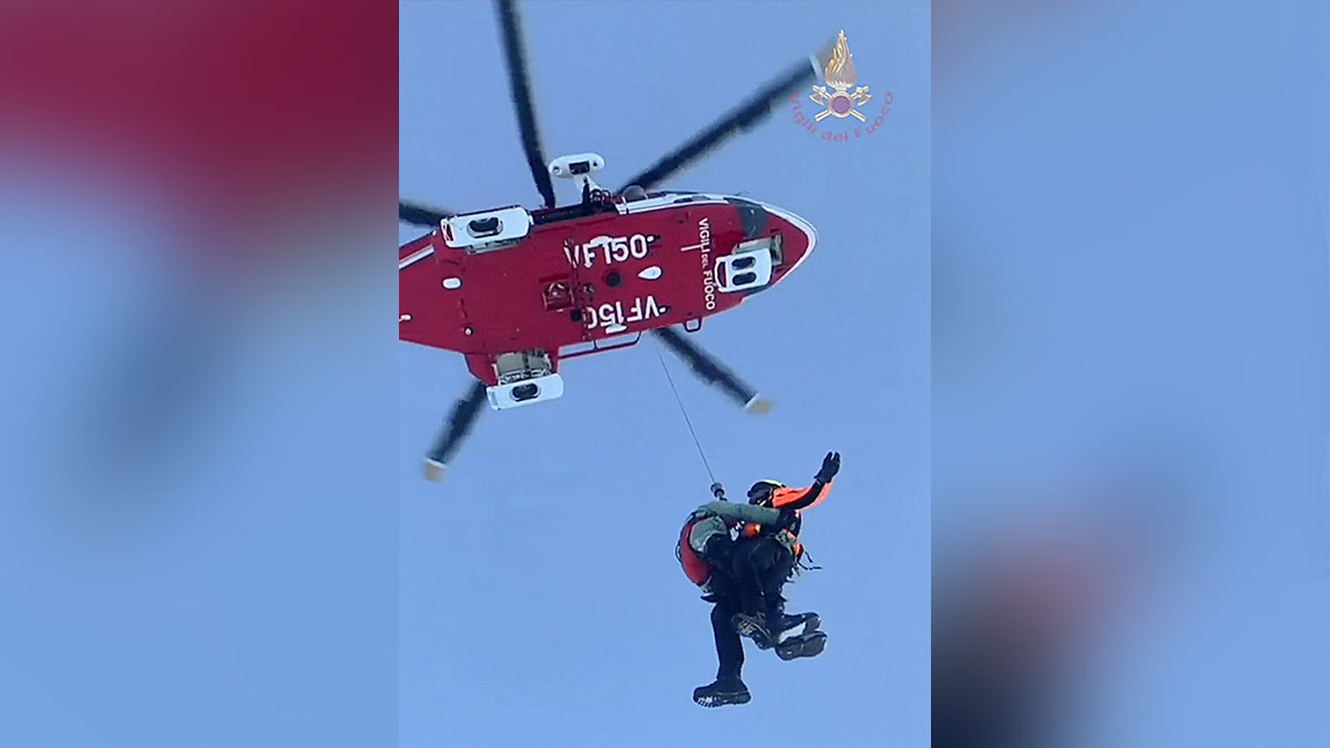 Vigili del Fuoco crew conducts helicopter rescue above snow-covered terrain.
