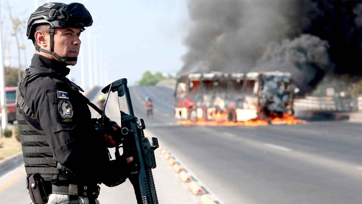 Officer stands near burning bus in Jalisco, Mexico.