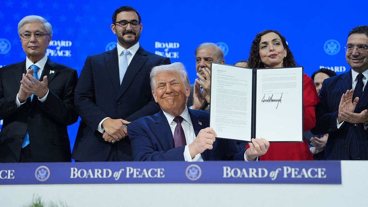 Donald Trump holding up a signed charter while standing in the center of a group.