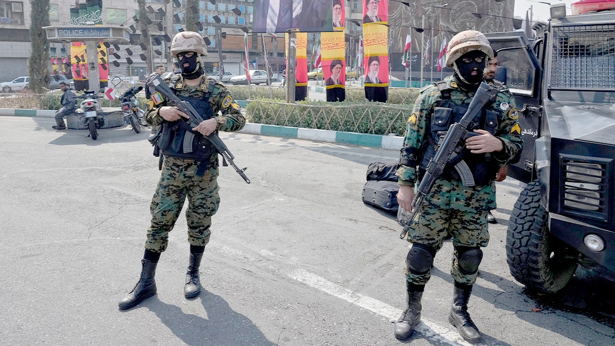 Iranian police officers stand near large banners displaying portraits of the late Supreme Leader Ayatollah Ali Khamenei in a public square in Tehran.