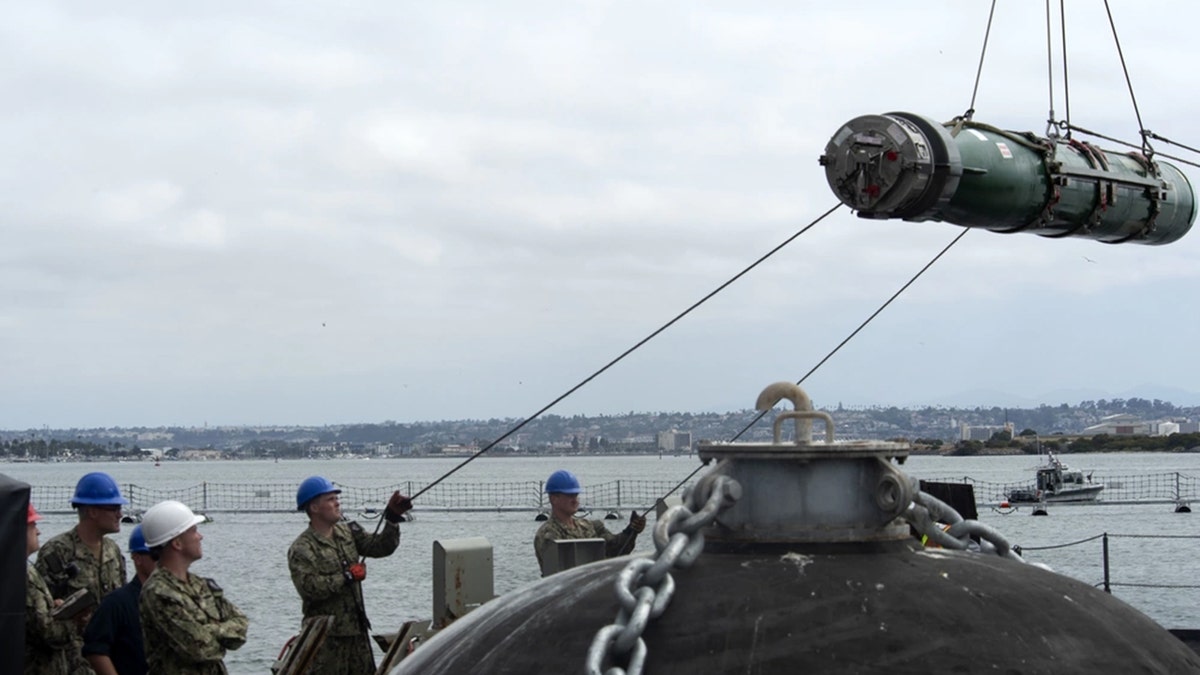 Sailors load torpedo on ship.
