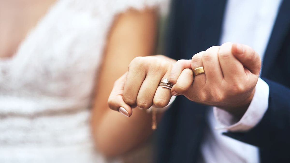 Newlywed couple making a pinky swear gesture showing wedding bands.