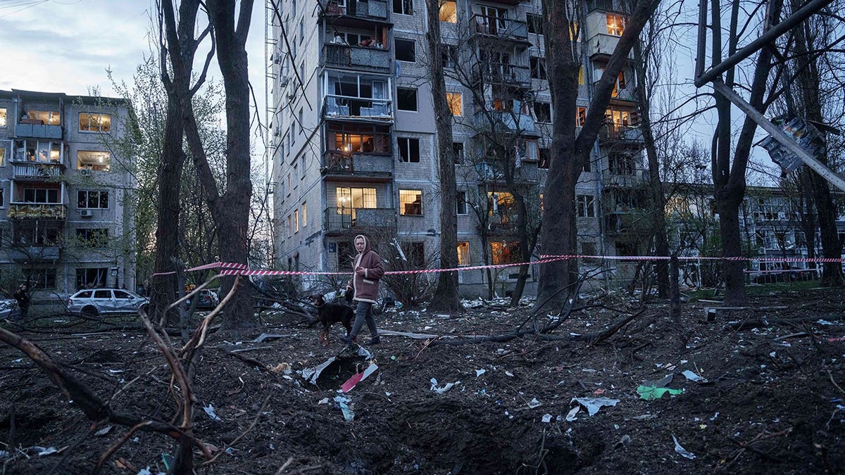 A woman and a dog walk through rubble.