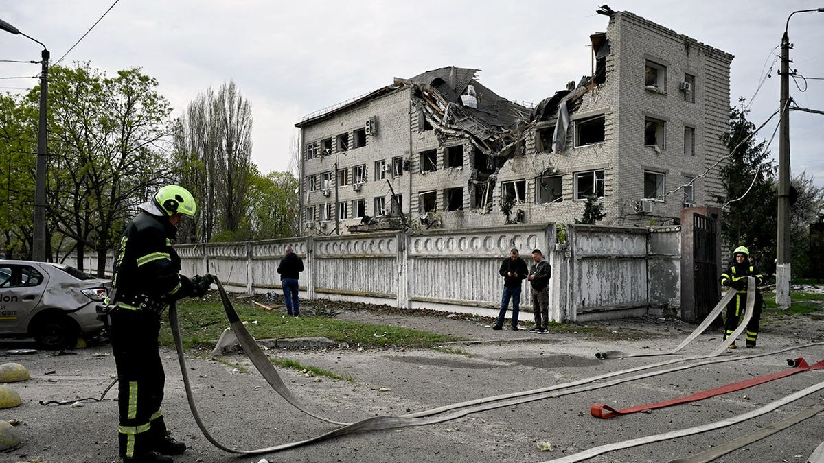 Firefighter stand with a hose in front of a crumbling building.