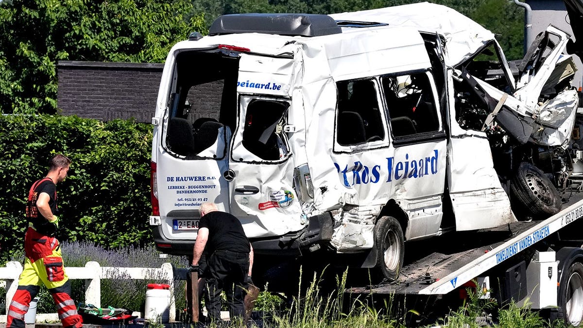 Emergency personnel moving a van onto a flatbed truck at a level crossing