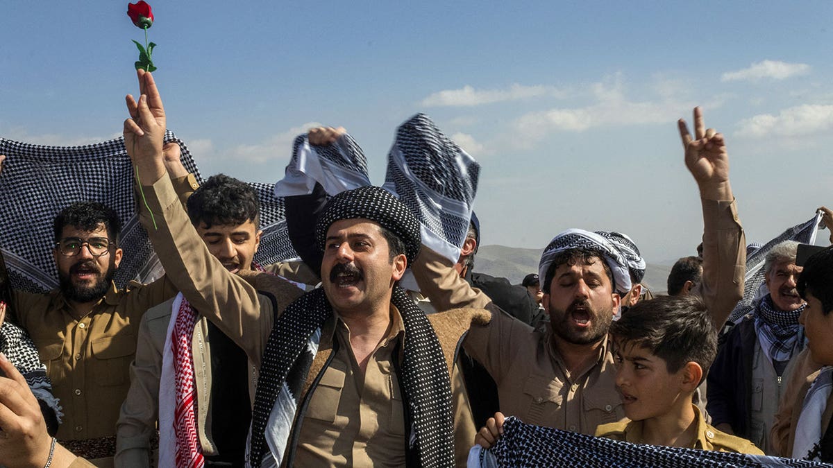 Men and women holding Kurdish scarves and roses during Nowruz festivities in Saqqez, Iran