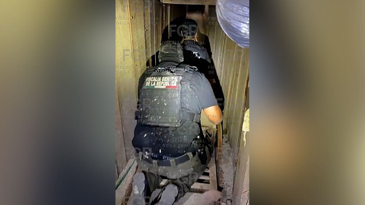 Mexican federal agents crawl through a narrow underground tunnel during a law enforcement operation.