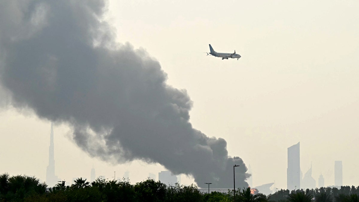 An Emirates aircraft flying past plumes of smoke near Dubai International Airport