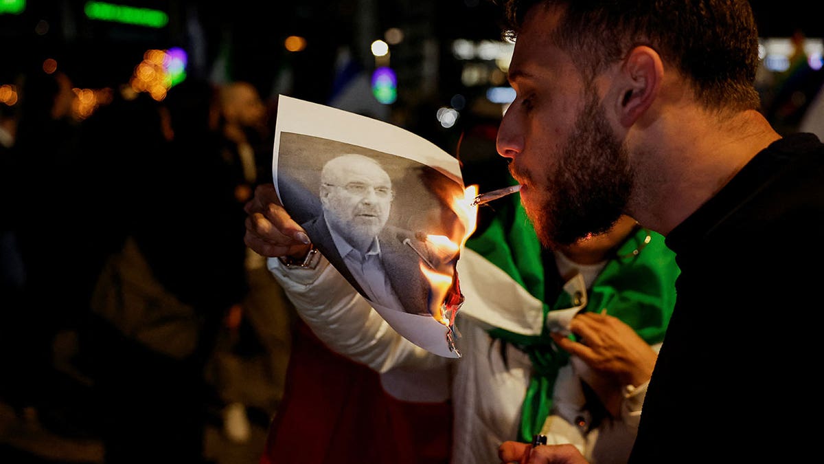 A man lighting a cigarette with fire from a burning picture of Iranian Parliament Speaker Mohammad Bagher Ghalibaf.