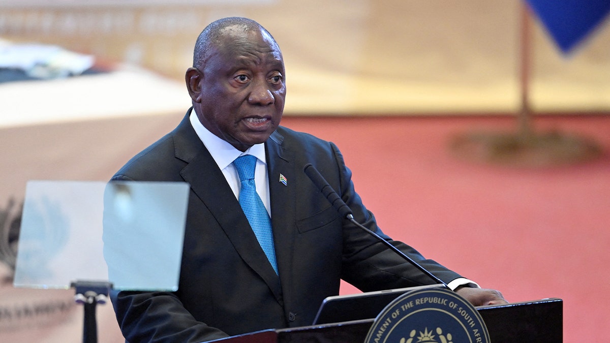 South Africa’s president speaks at a podium inside the parliamentary chamber during a nationally televised address.