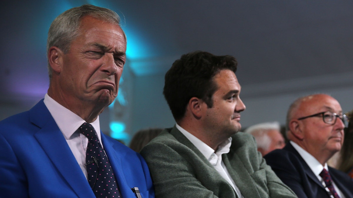 Reform leader Nigel Farage and Norfolk Police and Crime Commissioner candidate Colin Sutton (third left) listen and react to speeches at Holiday Inn on June 29, 2026 in Norwich, England. A by-election to choose the next Norfolk Police and Crime Commissioner (PCC) will be held on Thursday, 16 July 2026. The election was triggered by the resignation of former PCC Sarah Taylor due to a serious illness in her family. The by-election has sparked considerable debate, as it carries an estimated taxpayer cost of £2 million for a role that is scheduled to be abolished in 2028 when the regional devolution plans introduce a directly elected mayor for Norfolk and Suffolk.