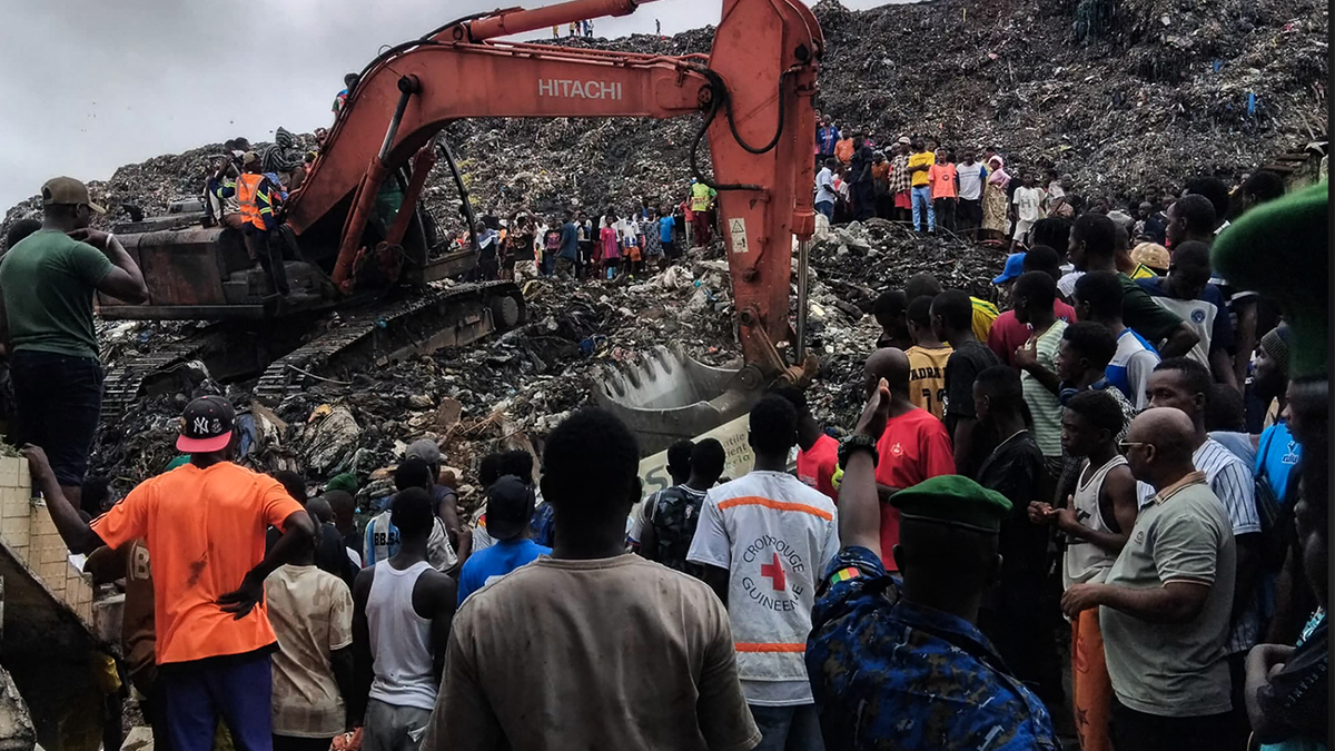 dozens of people at landfill with excavator