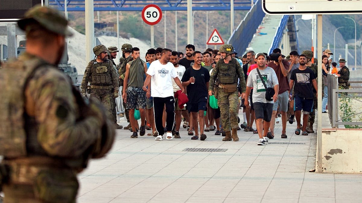 Migrants walk with Spanish army escorts returning to Morocco from Ceuta.