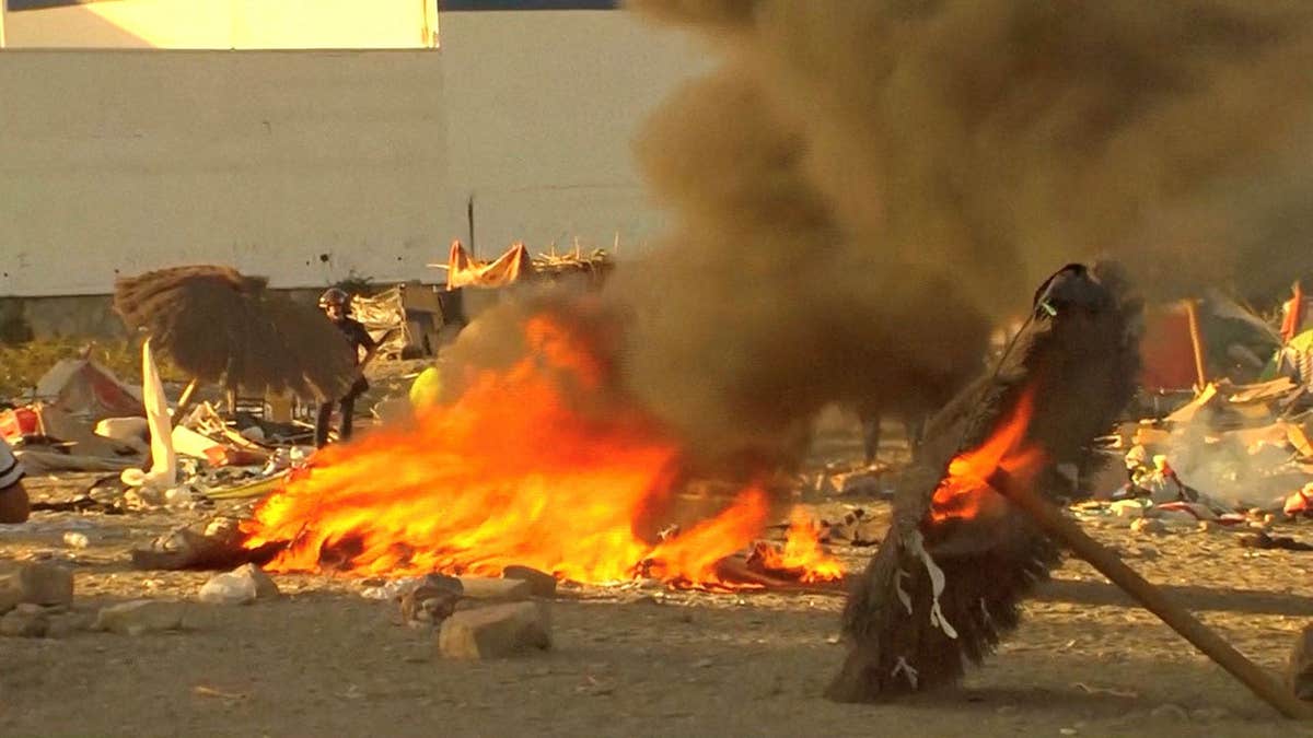 Law enforcement personnel stand while smoke and flames rise as Ceuta residents destroy migrant camp by the beach, in Ceuta, Spain
