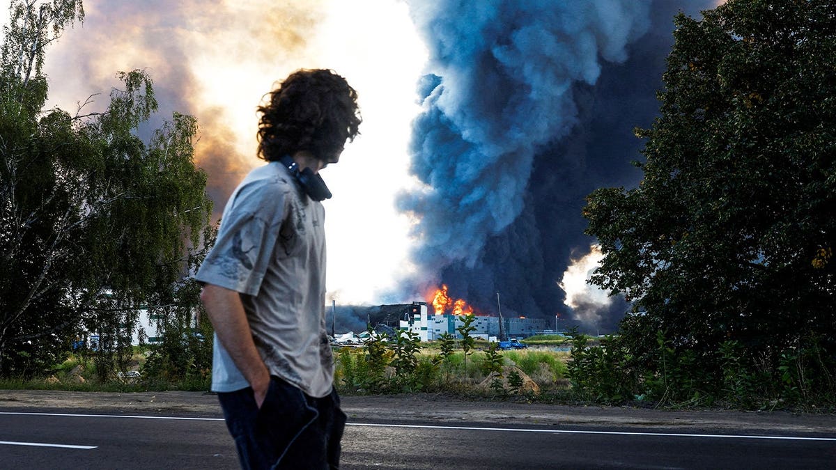 A man looks on as smoke rises over a warehouse, which was hit by a Russian drone strike, amid Russia's attack on Ukraine, in Kyiv region, Ukraine, August 27, 2026.