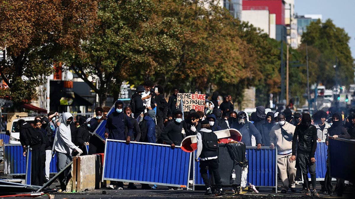 Masked protesters install a barricade amid clashes with police during a protest by high school students near the Lycee Berthelot high school in Aubervilliers near Paris