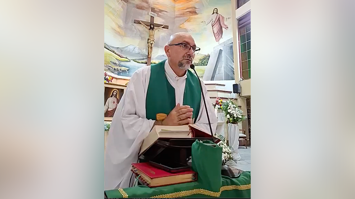 Father Patricio Alfredo Sánchez Molinari reads from a book during Mass with a large crucifix behind him