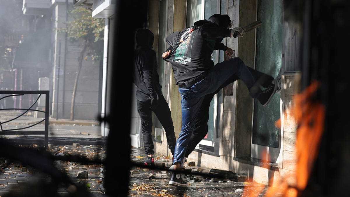 Hooded protesters smash a storefront window during clashes in Tirana, Albania.