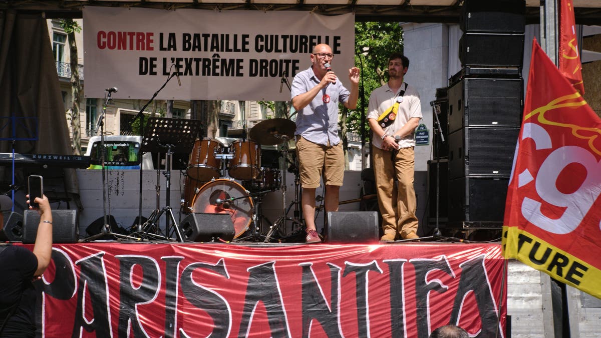 Speakers stand on a stage during a demonstration against Vincent Bollore's influence on culture in Paris.