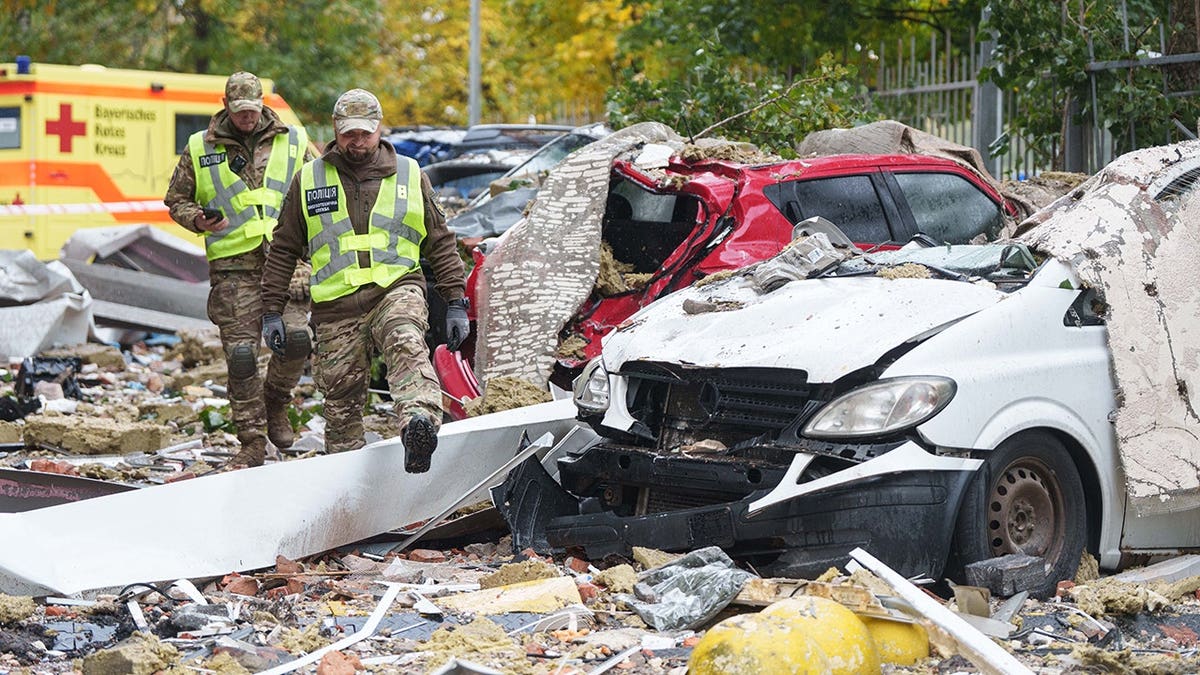 Policemen walk in front of destroyed cars in a damaged residential building yard in Kyiv.